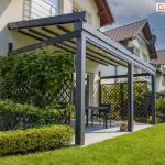 Aluminiowa pergola tarasowa Solid Selt z beżowym dachem rzymskim i antracytową konstrukcją oraz trejażami z roślinnością po bokach