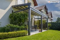 Aluminiowa pergola tarasowa Solid Selt z beżowym dachem rzymskim i antracytową konstrukcją oraz trejażami z roślinnością po bokach