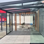 Drzwi przesuwne Miros zsunięte na bok, umożliwiające pełne otwarcie przestrzeni tarasu zabudowanego aluminiowym zadaszeniem ze szklanym dachem