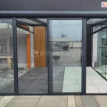 Szklane drzwi przesuwne Sotro w ciemnoszarej ramie aluminiowej, otwarte na boki z wszystkimi panelami zsuniętymi na środek konstrukcji. Konstrukcja systemu szklanego idealnie łączy funkcjonalność z minimalistycznym stylem.