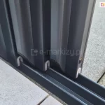 Zbliżenie na szyby zamontowane w przesuwnych panelach systemu Sotro, osadzonych w eleganckich, ciemnoszarych ramach aluminiowych. Panele płynnie przesuwają się na niezależnych torach prowadnicy.