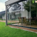 Tarasowe szklane drzwi przesuwne Miros zamontowane w eleganckiej konstrukcji ogrodowej, tworzące nowoczesną jadalnię na świeżym powietrzu z widokiem na ogród.