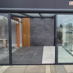 Zewnętrzne drzwi szklane Sotro w stylu loftowym, otwarte i przesunięte na prawą stronę konstrukcji. System przesuwny w eleganckiej, grafitowej ramie aluminiowej eksponuje przestronny taras i zapewnia przejście od frontu.
