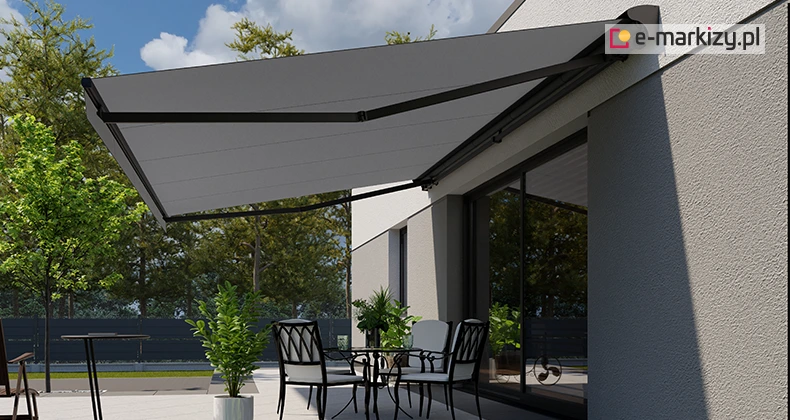 Stylowa markiza Jamaica Selt rozwinięta nad tarasem, przymocowana do jasnej elewacji budynku, osłania elegancki zestaw ogrodowy z czarnymi i białymi krzesłami.