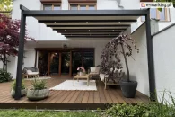 Nowoczesna antracytowa pergola tarasowa model Aura z trzema punktami LED na co drugiej belce, zamontowana na drewnianym tarasie z przytulną strefą wypoczynku i roślinnością w dużych donicach