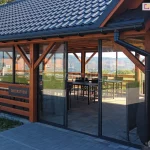 Drzwi przesuwne Sotro jako przeszklone wejście do drewnianej restauracji – system z ramowymi panelami szklanymi w konstrukcji ściennej
