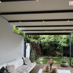 Nowoczesna pergola tarasowa Aura z rozsuwaną tkaniną w jasnym kolorze i zintegrowanym oświetleniem LED, tworząca eleganckie zadaszenie nad letnią strefą wypoczynku dla całej rodziny