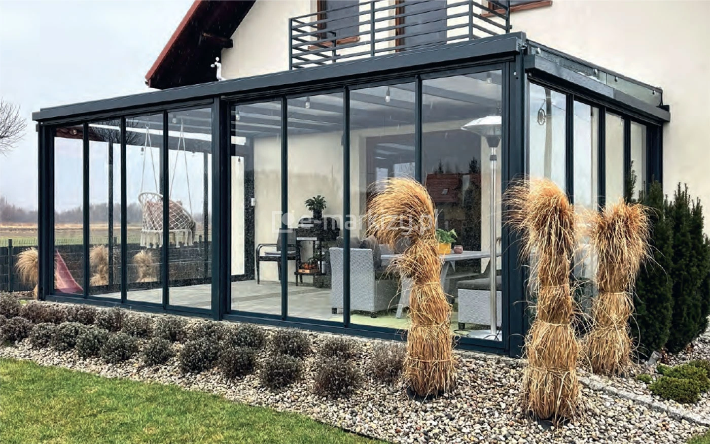Nowoczesna zabudowa tarasu systemem Sotro z przesuwnymi szklanymi panelami i aluminiową konstrukcją w ciemnym antracycie, zamontowana przy domu jednorodzinnym.
