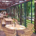 Zabudowa restauracji przesuwnymi drzwiami szklanymi Sotro z ramą – elegancka strefa jadalna z widokiem na zieleń przez przeszkloną ścianę umożliwiającą jedzenie na świeżym powietrzu i osłoniającą przed wiatrem