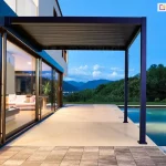 Nowoczesna pergola przeciwsłoneczna Gloria w kolorze antracytowym, montowana do elewacji domu nad wyjściem na taras z basenem. Idealne rozwiązanie na tarasy przy luksusowych domach z panoramicznym widokiem na góry i zieloną okolicę. Stylowe, minimalistyczne zadaszenie do strefy wypoczynkowej przy basenie.