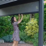 Opuszczana roleta screen z uchwytem do pergoli Gloria. Częściowo przejrzysta tkanina zapewnia prywatność bez zaciemniania.