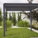 Lamelowa pergola aluminiowa Gloria do ogrodu z ręcznie sterowanym dachem umiejscowiona w narożniku przestrzennego ogrodu z miejscem na leżaki lub basen rozkładany