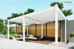 Nowoczesna biała pergola Marlo o szerokości 6 metrów przy żaluzjowym płocie w kolorze drewna. Zadaszenie ustawione na drewnianym podeście, wewnątrz wygodna narożna sofa i stoliki kawowe, tworzące przytulną strefę wypoczynkową.