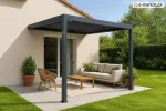 Pergola Marlo z ruchomymi żaluzjami dachowymi zamontowana na nasłonecznionym tarasie – nowoczesne i funkcjonalne zadaszenie przy domu chroniące przed słońcem miejsce wypoczynku z kanapą i stolikiem.