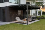 Pergola tarasowa Square Flat o szerokości 5 metrów z rozciągniętym dachem z tkaniny i zintegrowanym oświetleniem punktowym LED, zamontowana przy ciemnej elewacji nowoczesnego domu z żaluzjami fasadowymi, osłaniająca narożną sofę i leżak na tarasie ogrodowym z płyt gresowych, otoczona trawnikiem i ogrodem z brzozami.