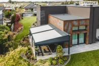 Wolnostojąca pergola ogrodowa Elegancy Tarasola o imponującej szerokości 9 metrów tworzy dużą przestrzeń wypoczynkową z sofami i stolikami, otoczoną nowoczesnym ogrodem i bujną roślinnością. Widok z góry podkreśla skalę konstrukcji oraz jej harmonijne dopasowanie do krajobrazu.