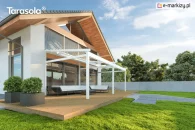 Luksusowa biała pergola aluminiowa Elegancy Tarasola z tkaninowym dachem rozpiętym nad dużą strefą wypoczynkową podkreśla nowoczesny design tarasu. Konstrukcja stoi obok domu na drewnianej platformie, otoczonej zadbaną zielenią i minimalistycznym ogrodzeniem