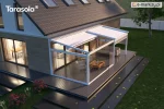 Biała pergola z rozwijanym dachem tkaninowym Elegancy Tarasola zabudowana szkłem tworzy elegancki ogród zimowy z wygodną sofą i stolikiem. Transparentne panele otwierają widok na ogród z drzewami i trawnikami, przepuszczając naturalne światło o zachodzie słońca.