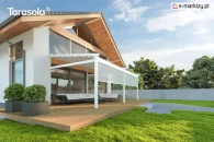 Tkaninowa biała pergola Elegancy Tarasola z rozwijanymi roletami frontowymi osłania strefę relaksu z narożnym zestawem wypoczynkowym na drewnianym tarasie. Konstrukcja łączy się wizualnie z nowoczesną architekturą domu, a w tle znajdują się drzewa i ogrodzenie.