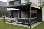 Rzymska pergola tarasowa Square Flat firmy MOL z antracytową aluminiową konstrukcją i zamkniętym dachem z tkaniny oraz oświetleniem LED, zamontowana przy elewacji białego domu z dużymi przeszkleniami i żaluzjami zewnętrznymi. Na tarasie narożna sofa ogrodowa, leżak z poduszką, grill i meble wypoczynkowe na betonowej posadzce otoczonej zadbanym trawnikiem.
