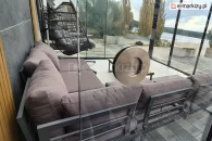 Dwustronny, aluminiowy uchwyt zamontowany w panelu szklanym systemu Auris, umożliwiający wygodne otwieranie i zamykanie drzwi tarasowych. W tle widoczne przesuwne przeszklenia, narożna sofa ogrodowa oraz widok na jezioro i nowoczesny taras z płytkami gresowymi