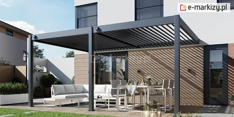 Pergola Rubio Soft z ręcznie sterowanym dachem lamelowym tworzy elegancką osłonę tarasu, zapewniając precyzyjną regulację światła. Aluminiowa konstrukcja w antracytowym kolorze prezentuje się nowocześnie, a lamele rzucają dekoracyjne, równoległe cienie na jasną elewację domu. Całość uzupełnia uporządkowana strefa wypoczynkowa na drewnianym podeście otoczona ogrodem.