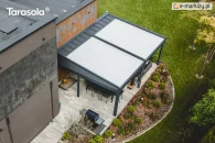 Wolnostojąca podwójna pergola Elegancy Tarasola z dużym tkaninowym dachem ustawiona obok budynku, zapewnia obszerną przestrzeń wypoczynkową z sofami i stołem na eleganckim tarasie. Widok z góry ukazuje jej skalę i dopasowanie do ogrodu z bujną roślinnością oraz geometrycznymi rabatami.