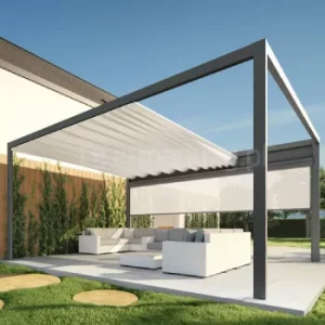 Wolnostojąca pergola Tarasola Flat o prostokątnej konstrukcji aluminiowej z rozwijaną, rzymską tkaniną dachu oraz boczną roletą zip i rynną odpływową osłania białą strefę wypoczynkową na tarasie. Konstrukcja stoi niezależnie od budynku, na dużych płytach tarasowych, otoczona trawnikiem i nowoczesnymi nasadzeniami przy ścianie domu.