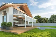 Tkaninowa biała pergola Elegancy Tarasola z rozwijanymi roletami frontowymi osłania strefę relaksu z narożnym zestawem wypoczynkowym na drewnianym tarasie. Konstrukcja łączy się wizualnie z nowoczesną architekturą domu, a w tle znajdują się drzewa i ogrodzenie.