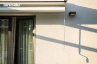 Zbliżenie na ręczną korbę służącą do rozwijania tkaninowego dachu pergoli Tarasola Simple montowanej do ściany.