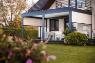 Pergola Essential z roletami bocznymi tworząca przytulną, osłoniętą strefę wypoczynkową na tarasie domu jednorodzinnego