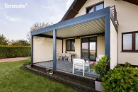 Duża pergola tarasowa Essential z zabudowanymi bokami jako funkcjonalna przestrzeń relaksu, otoczona roślinnością i ogrodową zielenią