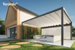 Wolnostojąca pergola Tarasola Flat z prostokątną konstrukcją aluminiową i falowaną tkaniną przeciwdeszczową tworzy eleganckie zadaszenie nad zestawem wypoczynkowym. Konstrukcja stoi niezależnie od budynku, na dużej, jasnej płycie tarasowej, a całość otacza nowoczesny ogród z dekoracyjnymi drewnianymi stopniami i pnączami na ścianie domu.