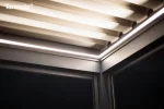 Podświetlenie ukryte w konstrukcji pergoli Tarasola Essential rozjaśnia wieczorne przestrzenie tarasu, tworząc przytulny klimat pod lamelowym dachem. Minimalistyczna forma aluminiowych profili subtelnie kontrastuje z ciemnym niebem, a otaczająca zieleń dodaje całości naturalnej harmonii.