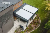 Wolnostojąca podwójna pergola Elegancy Tarasola z dużym tkaninowym dachem ustawiona obok budynku, zapewnia obszerną przestrzeń wypoczynkową z sofami i stołem na eleganckim tarasie. Widok z góry ukazuje jej skalę i dopasowanie do ogrodu z bujną roślinnością oraz geometrycznymi rabatami.