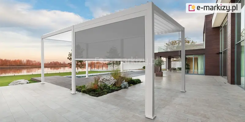 Pergola tarasowa z roletą screen Gloria, aluminiowa konstrukcja w jasnej, białej kolorystyce z boczną osłoną przeciwsłoneczną i wiatrochronną, nowoczesna zabudowa tarasu przy domu z widokiem na ogród i zbiornik wodny, zapewniająca ochronę przed słońcem, wiatrem oraz zwiększająca prywatność strefy wypoczynku.