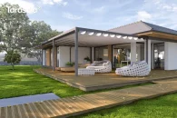 Szeroka pergola Tarasola Flat na 6 nogach z tkaninowym dachem i prostokątną aluminiową ramą osłania przestronny taras wypoczynkowy z designerskimi fotelami oraz drewnianym podestem. Konstrukcja stoi niezależnie od budynku, otoczona dużym trawnikiem i ogrodem.