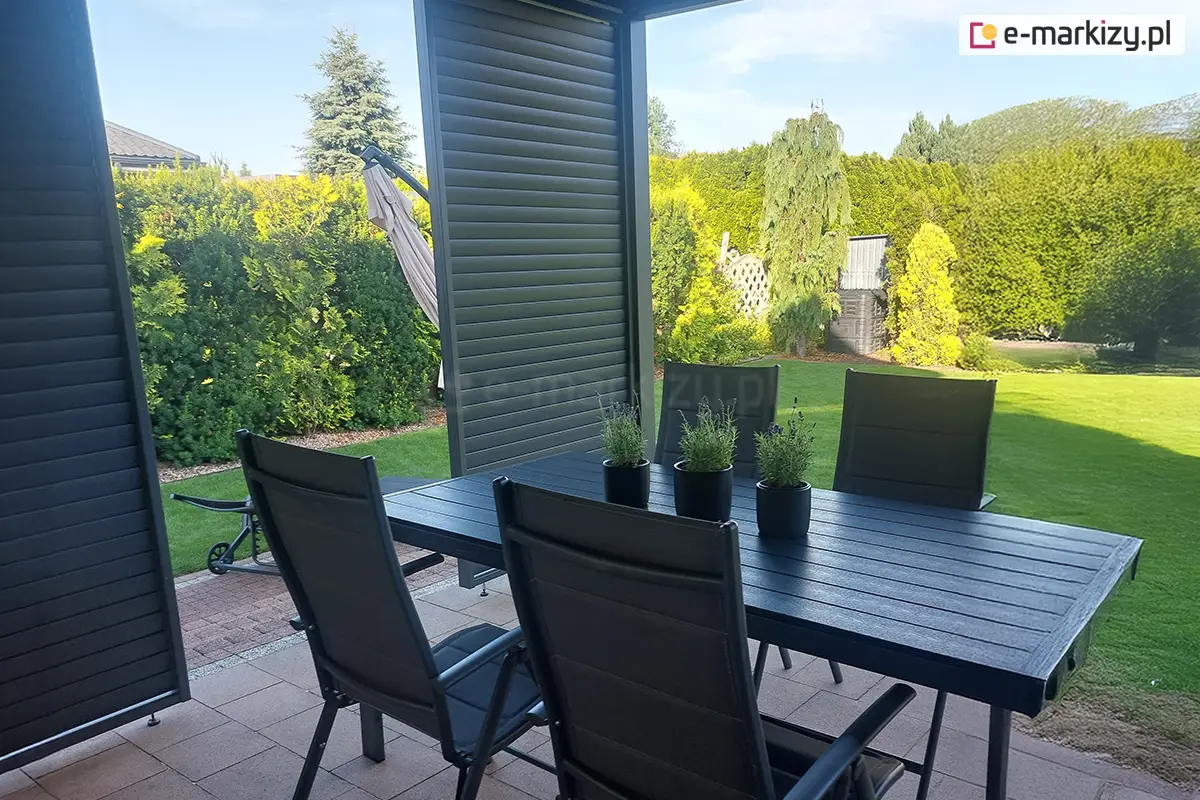 Zestaw mebli ogrodowych pod zadaszeniem tarasu z ruchomymi żaluzjami bocznymi zapewniającymi prywatność i ochronę przed słońcem.