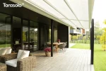 Tarasola Light zadaszenie tarasu z tkaniny Opatex w kolorze białym, rozwijany wodoodporny dach przeciwsłoneczny nad drewnianym tarasem przy nowoczesnym domu, minimalistyczna pergola przyścienna z aluminiową konstrukcją i jednospadowym dachem zwijanym.